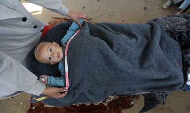 An aerial view of a baby under a blanket, with two hands measuring the blanket.