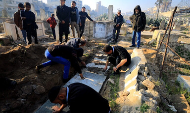 Men stand and sit next to white casket lowered into the ground