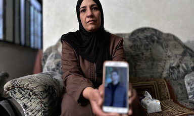 A woman holds out a phone with a picture of her son