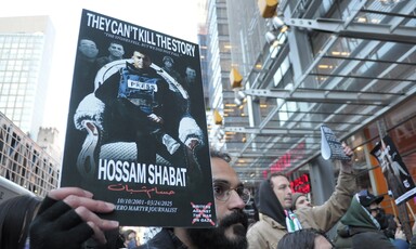 Man holds poster showing Hossam Shabat in press jacket sitting in armchair