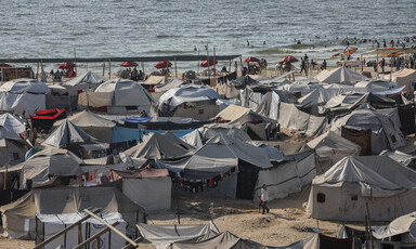 Dozens of tents are set up on the sand, with a view of the ocean in the background.