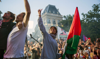 Woman wearing gray sweatshirt smiles while looking up and holding fist up in the air in front of massive crowd