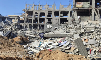 Landscape view of skeleton of badly damaged mid-rise building with rubble strewn in front
