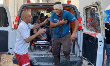 A bandaged man and a paramedic outside the back of an ambulance