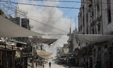 A person walks on a road as a a giant plume of gray smoke clouds the horizon in front of them.