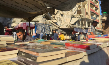 A  pile on the books in the foreground and man apparently reading behind