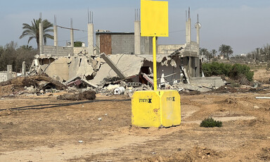 A concrete block painted yellow with a yellow sign stands before the rubble of buildings