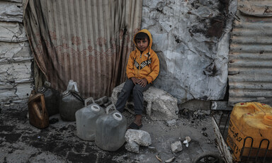 A child sits on a stone with four jugs at his feet. 