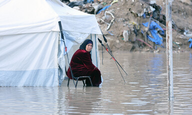 Woman in red dress looks toward camera while sitting on chair with water up to her calves