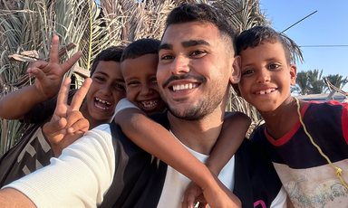 Three children and a young man huddle together smile for the camera on a sunny day.