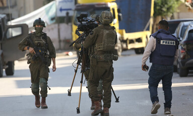 three soldiers surround a camera as a man in press vest looks on