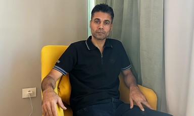 A man in a black collared shirt sits in a yellow chair. 