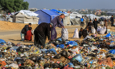 Palestinian adults and children sort through garbage at a landfill north of Khan Younis with tents in the background