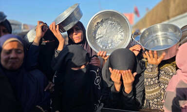 Women holding empty metal bowls look fatigued as they stand in the sun