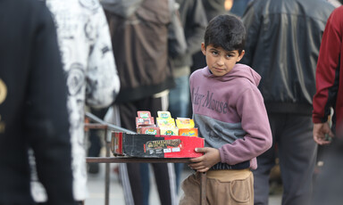 A boy wearing a Mickey Mouse sweatshirt holds a tray of goods.
