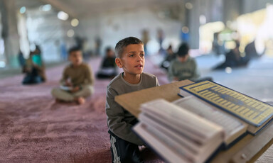 A boy sits before a Quran, pages open, reciting. 
