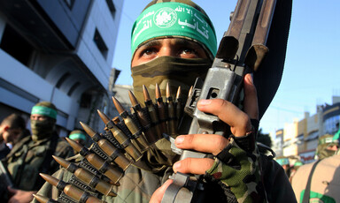 Close-up of young man with covered face wearing green headband and carrying a gun