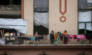 Two girls are standing on a scarred building's threshold where clothes are hung on clotheslines