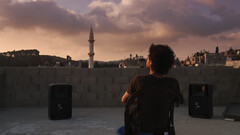 Man sits on chair overlooking city at sunset