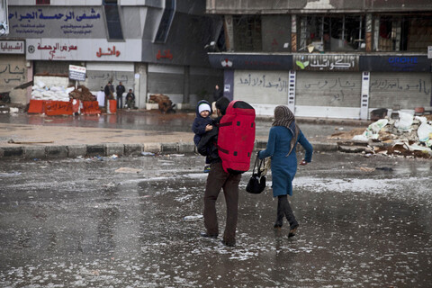 Couple carrying baby cross flooded street in war-torn camp