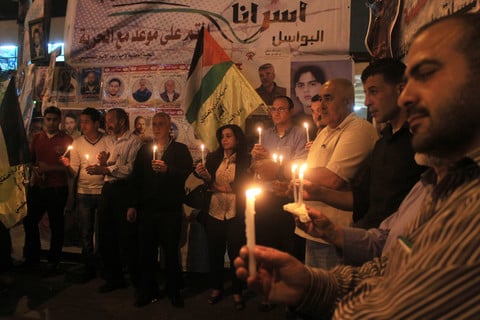 Crowd hold candles in tent covered with posters of political prisoners