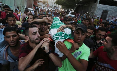 Youth wrapped in funeral shroud is carried on the shoulders of young men in crowded procession