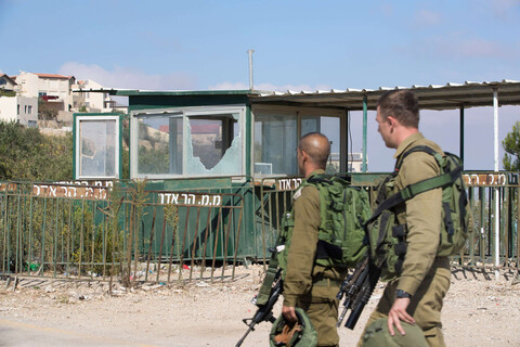 Two soldiers carrying heavy weaponry walk in front of checkpoint with shattered windows