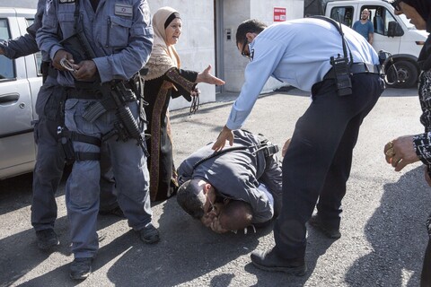 Elderly woman gestures her arm towards police officer as he stands over another officer who has pinned man to the ground