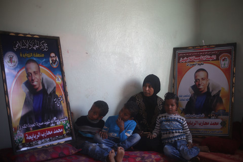 Woman and three small children sit on floor next to two large posters of smiling young man