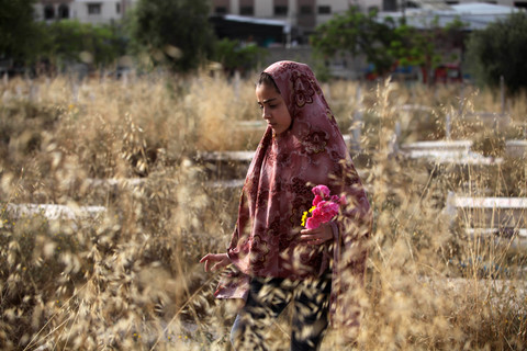 Woman wearing headscarf holds flowers in a wheat field