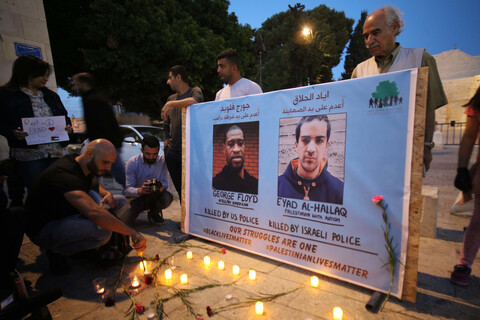 Man lights candles before banner with two portraits of men