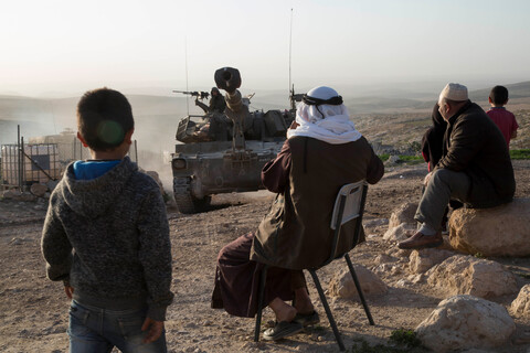 Villagers watch an approaching military vehicle  