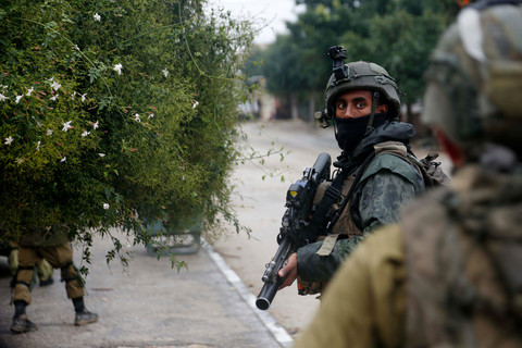A soldier carrying a rifle looks at camera while standing on street