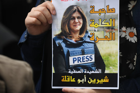 Close-up of a hand holding a poster of Shireen Abu Akleh wearing a press vest