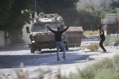 Young man with his  arms in the air stands in front of military vehicle