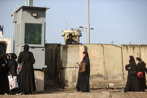 Woman walk in front of concrete barriers with armed Israeli soldiers standing above them