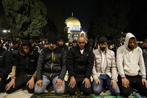 A group of mean kneels in prayer with golden dome behind them