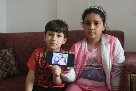 A boy and a girl sit on a sofa holding a mobile phone 