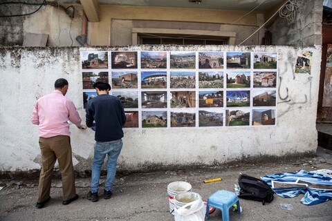 Two men put up photos on a white wall