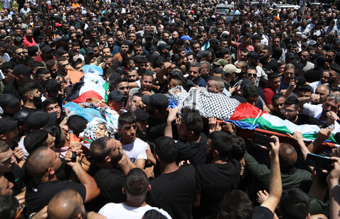 A crowd of dozens carry two bodies on stretchers wrapped in Palestine flags and kuffiyehs