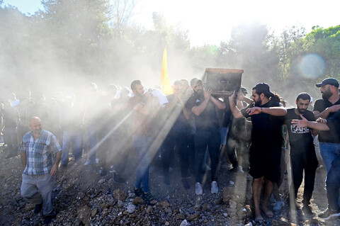 Sunlight streams over the shoulders of young men carrying a coffin