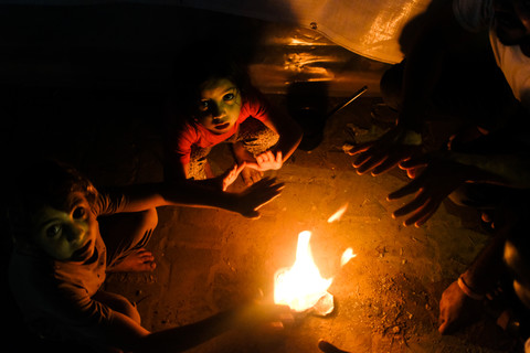A man and two children warm themselves by a fire