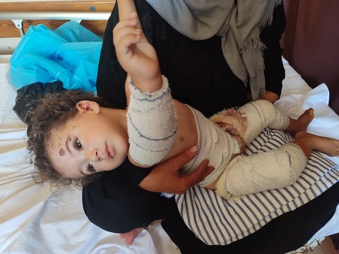 An injured child held by a woman sitting on a hospital bed 