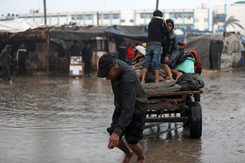 A bare-footed man wearing a baseball cap pulls a loaded cart carrying multiple children