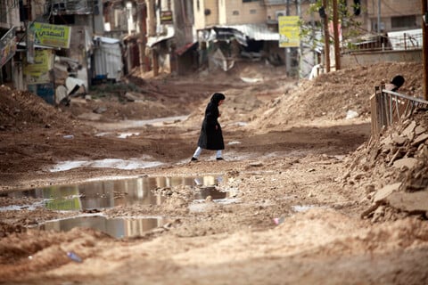 A girl walks amid muddy, damaged roads 