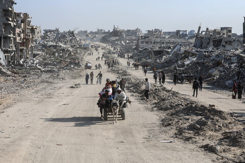 A cart traverses a dust road in a bleak landscape of destroyed buildings