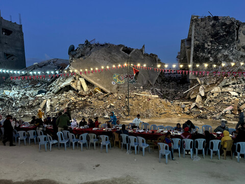 People gather under festive lights on a background of destroyed buildings