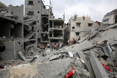 People stand on the top of piles of rubble. Some of them are wearing orange vests.