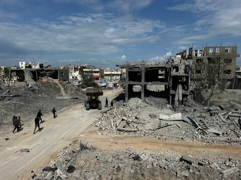 During the daytime, a road runs through bombed-out buildings.