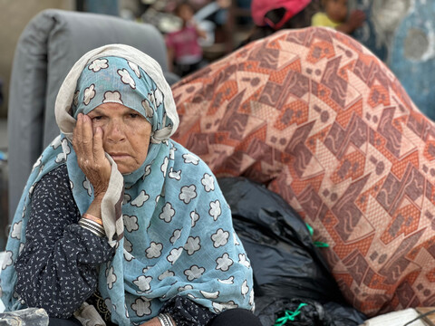 An older woman hold her head in her right hand while sitting in front of personal belongings